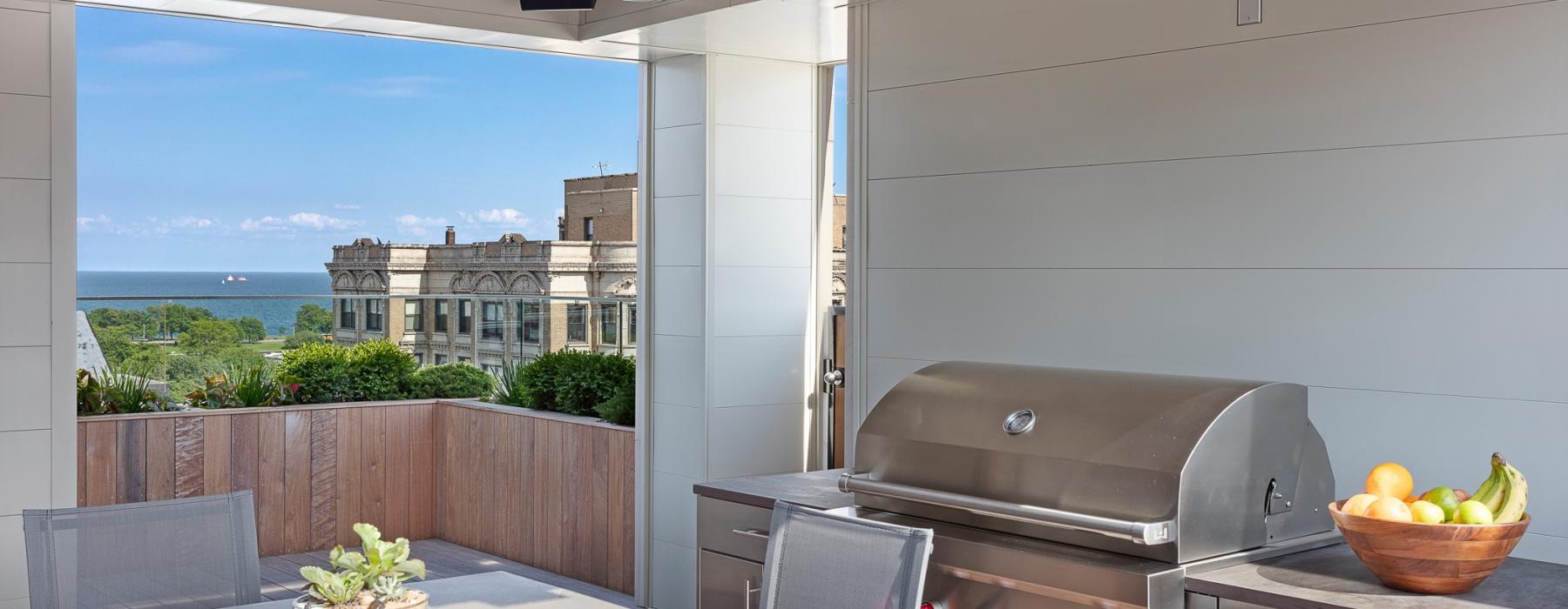 a rooftop patio with a grill and a table with a bowl of fruit